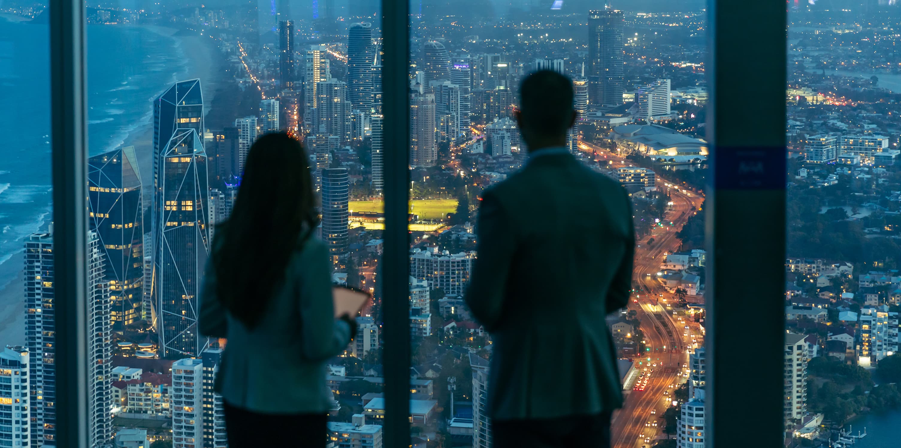 Two business people looking at the view from a building at night.