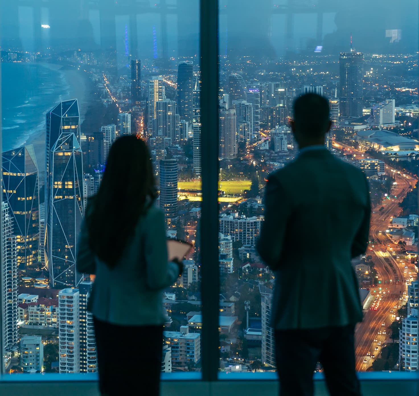 Two professional people look out of the windows of Q1 at the city below.