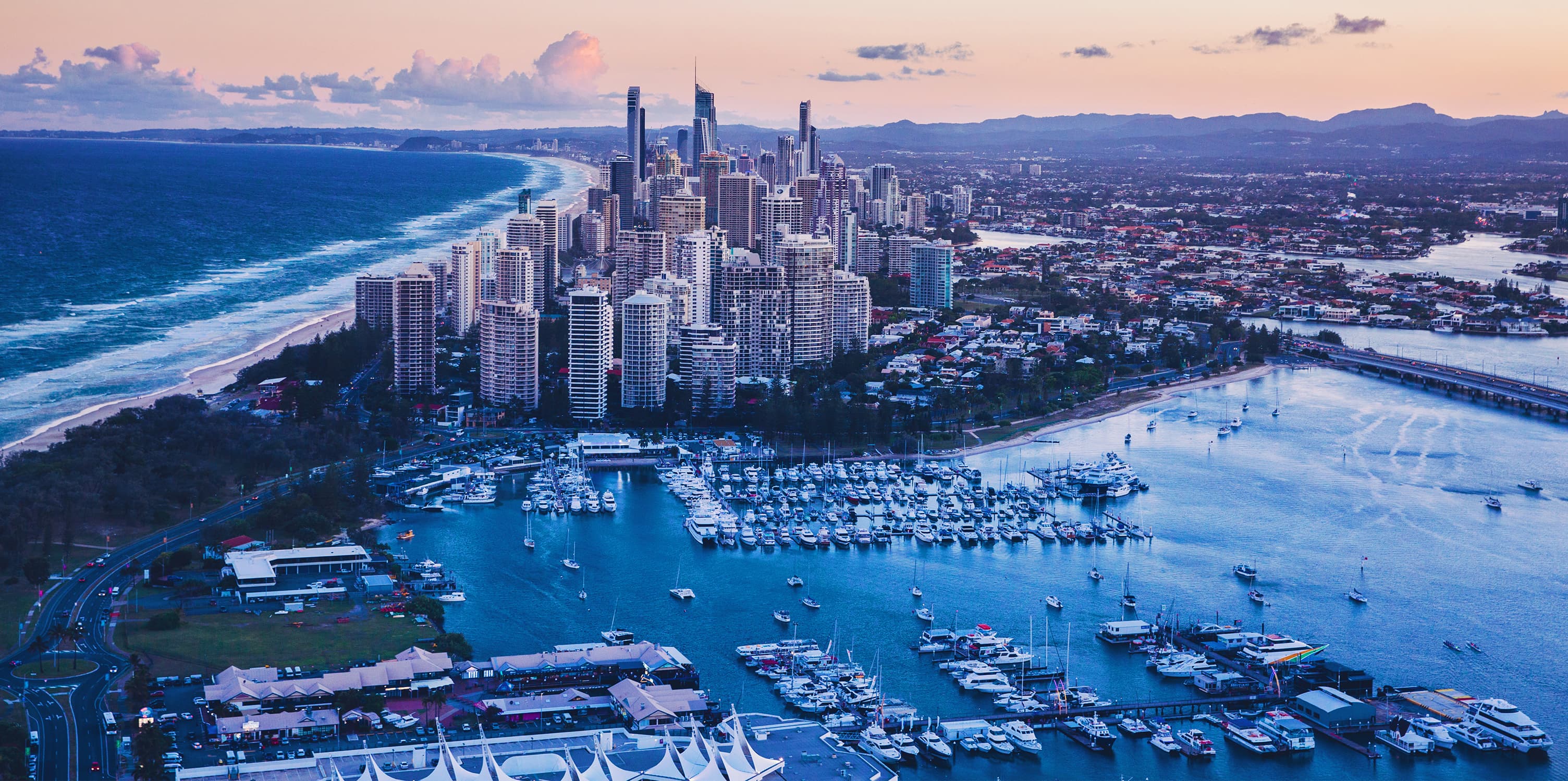 Aerial view of the water and city skyline of the Gold Coast at sunset.